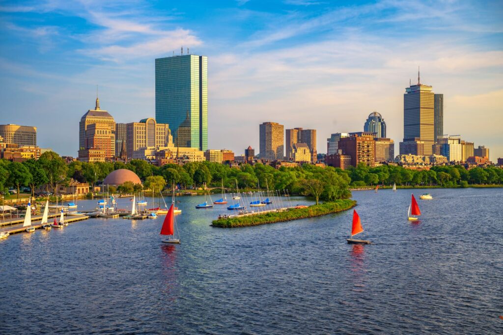 Segelbåtar på Charles River med Bostons skyline och träd längs stranden i bakgrunden