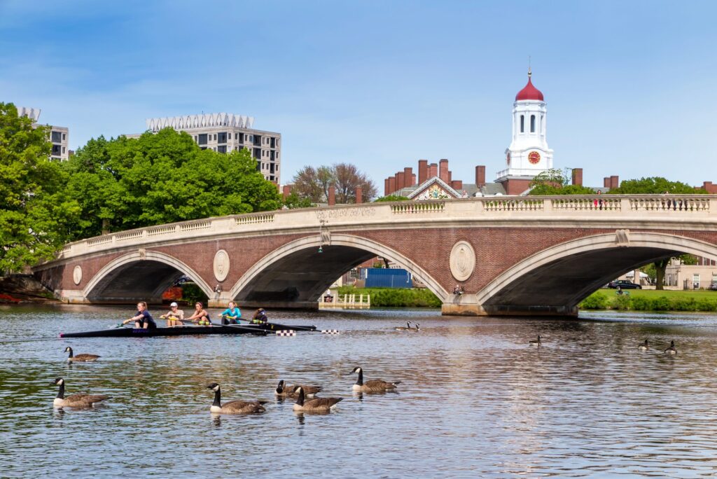 Tegelbro med valv över Charles River med träd och ett torn i Cambridge bakom