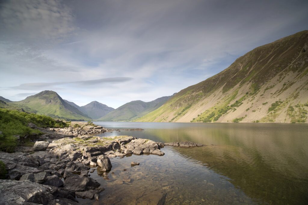 Klippig sjöstrand och branta sluttningar under moln i Lake District