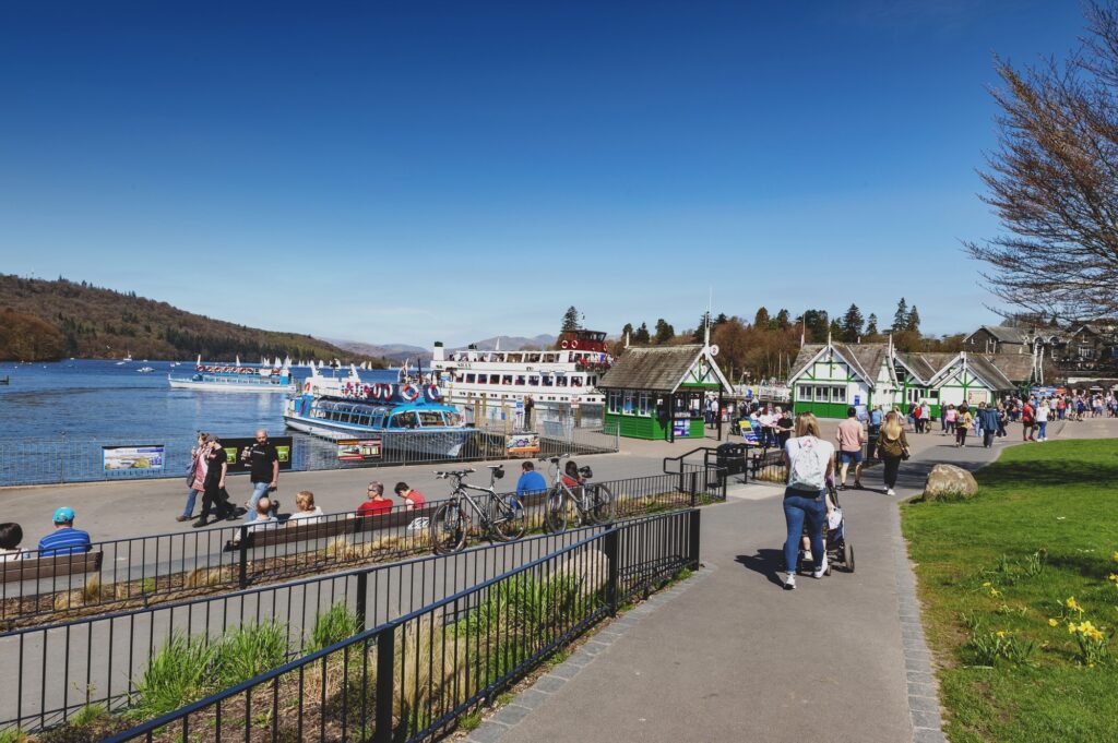 Människor på strandpromenaden i Bowness-on-Windermere med en båt på sjön