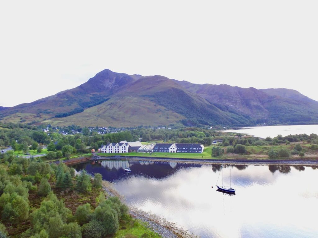 The Isles of Glencoe Hotel vid stilla vatten med berg i bakgrunden