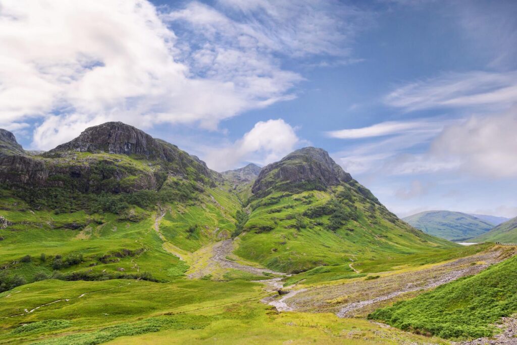 Gröna bergssluttningar och en väg i dalen nedanför Three Sisters i Glencoe