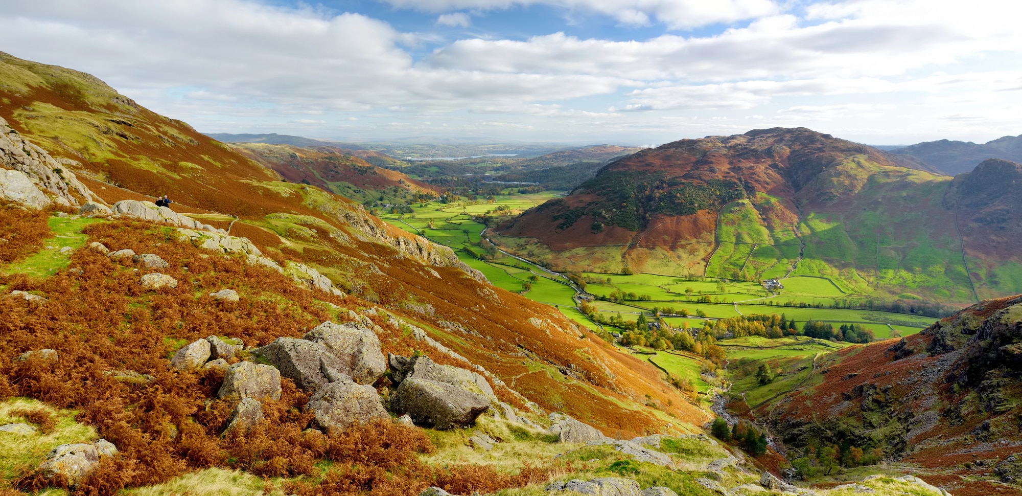 Klippig sluttning med höstfärgad ormbunke ovanför en grön dal och kullar i Lake District