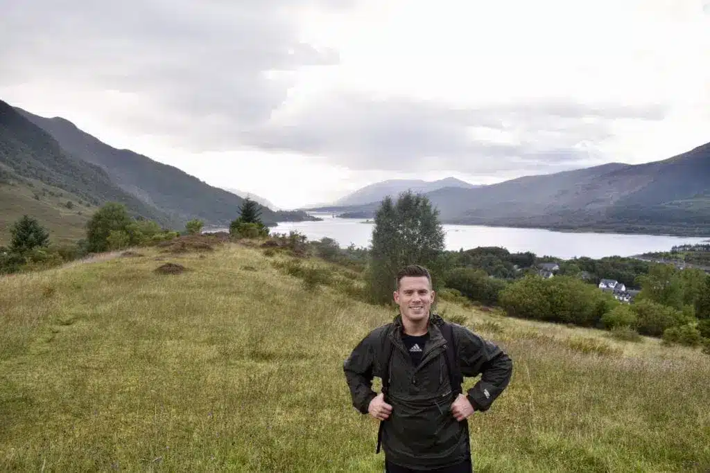 En vandrare på en gräsbevuxen stig med en sjö och berg i bakgrunden