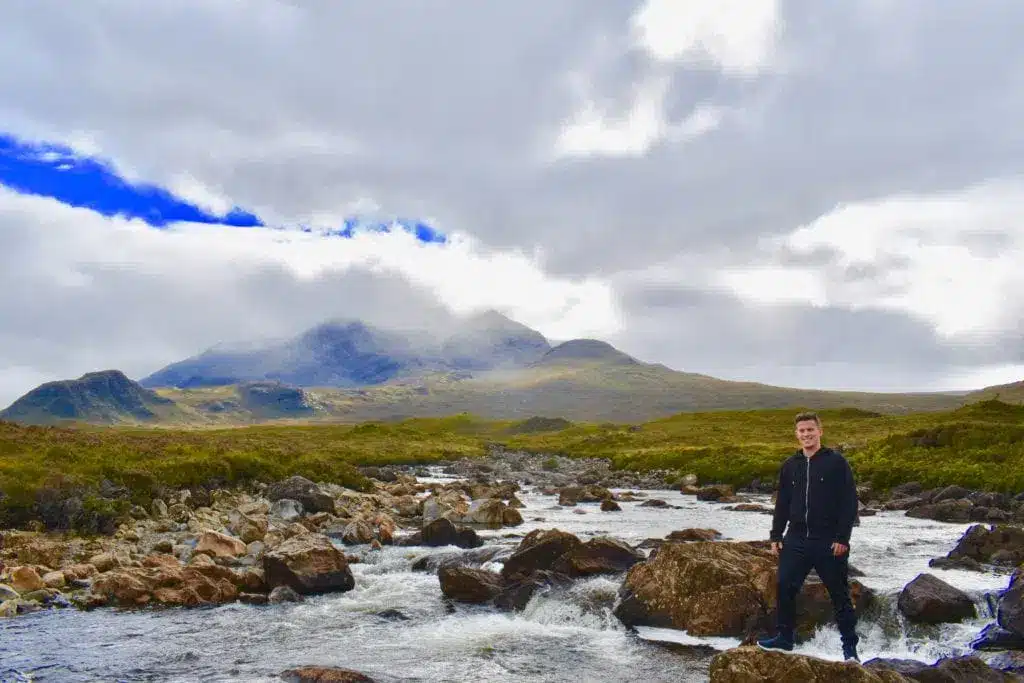 En vandrare vid en stenig bäck med berg i bakgrunden på Isle of Skye