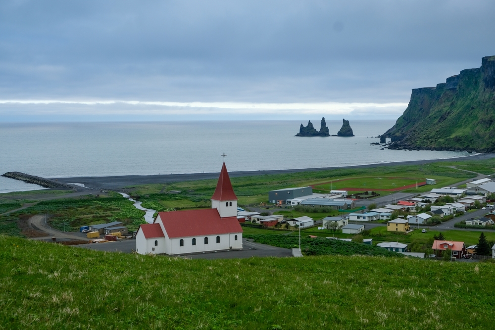 Vík med kyrkan, den svarta stranden och klipporna Reynisdrangar på Islands sydkust