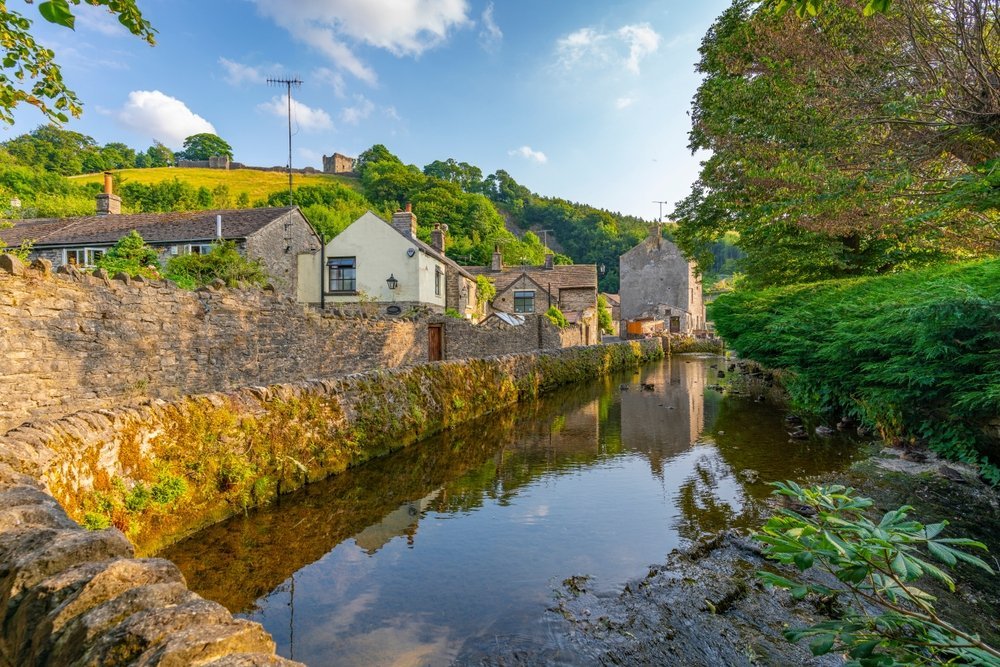 Byn Castleton och bäcken med ruinen av Peveril Castle ovanför husen