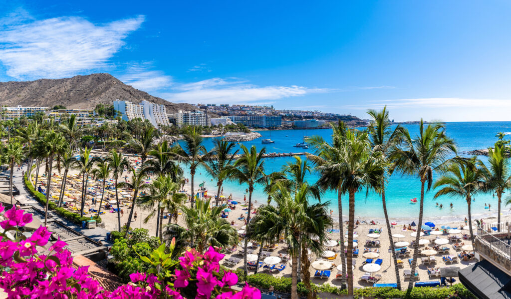 Stranden vid Anfi del Mar på Gran Canaria med palmer, parasoller och turkosblått vatten