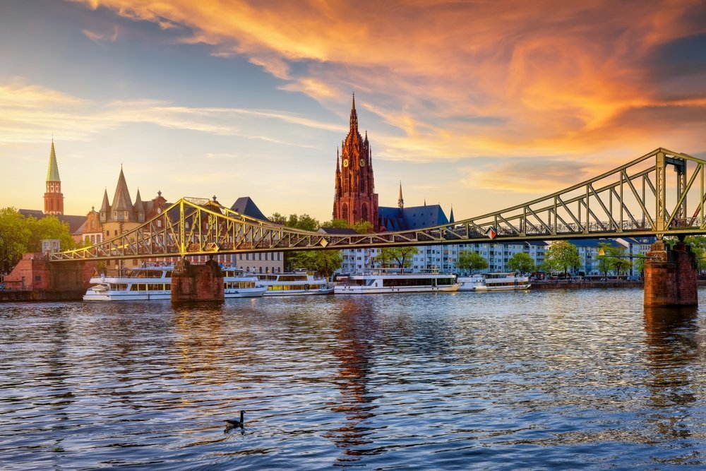 Frankfurts skyline med gångbron Eiserner Steg och Kejsardomen över Main i solnedgången